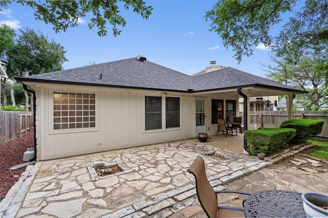 rear view of property featuring a patio, fence, roof with shingles, and an outdoor fire pit