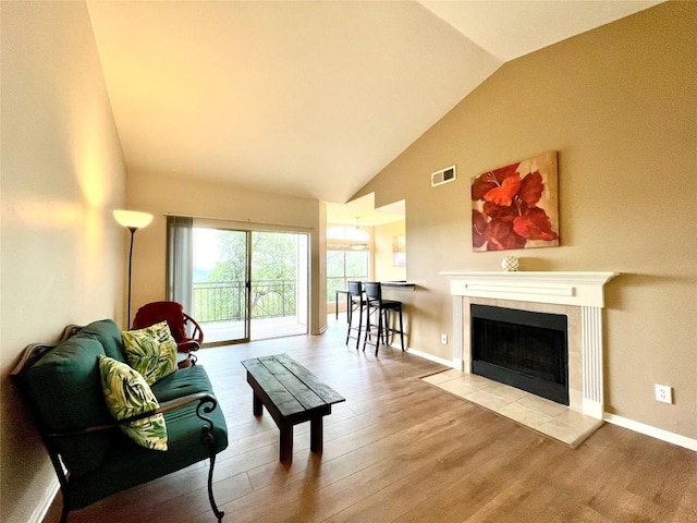 living room featuring a fireplace, high vaulted ceiling, baseboards, wood finished floors, and visible vents