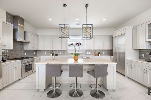 kitchen featuring premium appliances, a breakfast bar, a center island with sink, and wall chimney exhaust hood