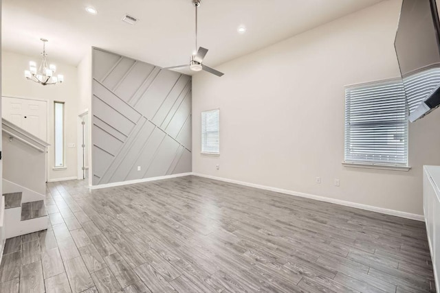 unfurnished living room with visible vents, baseboards, ceiling fan with notable chandelier, and wood finished floors