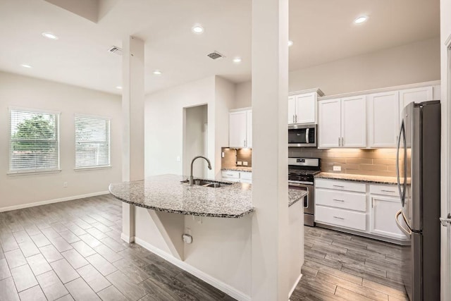kitchen featuring decorative backsplash, a sink, white cabinets, light wood finished floors, and stainless steel appliances