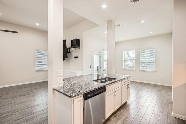 kitchen featuring wood finished floors, white cabinets, light stone counters, a sink, and dishwasher