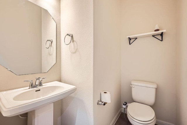 half bath featuring baseboards, a sink, and toilet