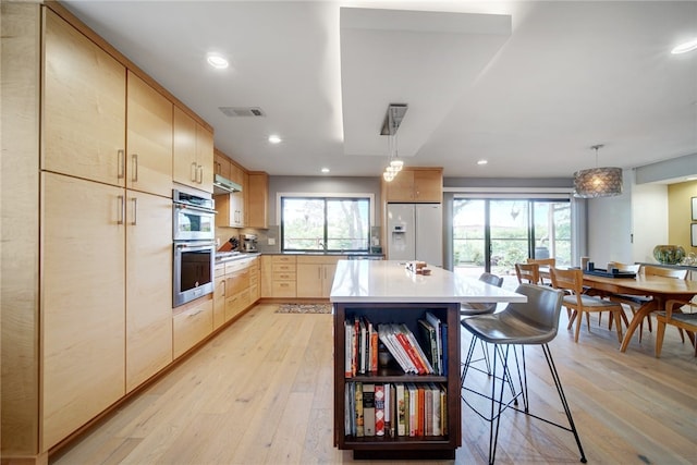 4411 Bilboa Dr, Austin, TX 78759 - kitchen with light brown cabinets, stainless steel appliances, a breakfast bar area, light wood finished floors, and healthy amount of natural light