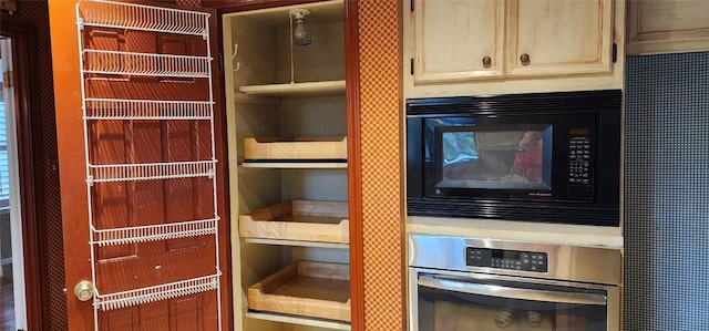 interior details featuring cream cabinetry, stainless steel oven, and black microwave