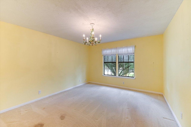 empty room featuring a textured ceiling, baseboards, an inviting chandelier, and light carpet