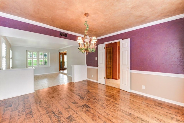 spare room with visible vents, crown molding, wood finished floors, baseboards, and a chandelier