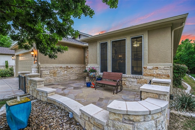 712 Independence Creek Ln, Georgetown, TX 78633 - back of house at dusk featuring an attached garage, stucco siding, stone siding, and a patio
