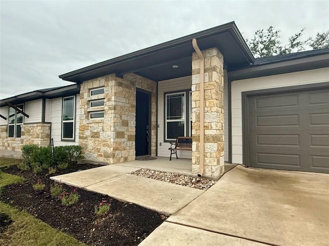 doorway to property with a garage, concrete driveway, a porch, and stone siding