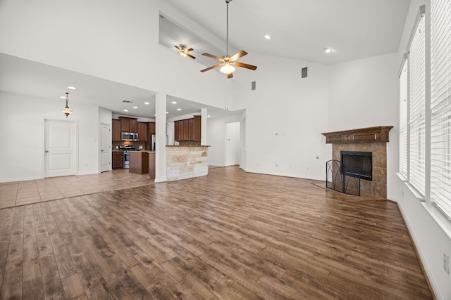 unfurnished living room featuring visible vents, ceiling fan, high vaulted ceiling, a tile fireplace, and dark wood finished floors