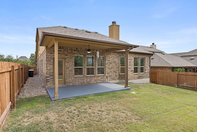 back of property featuring brick siding, a fenced backyard, a ceiling fan, and a chimney