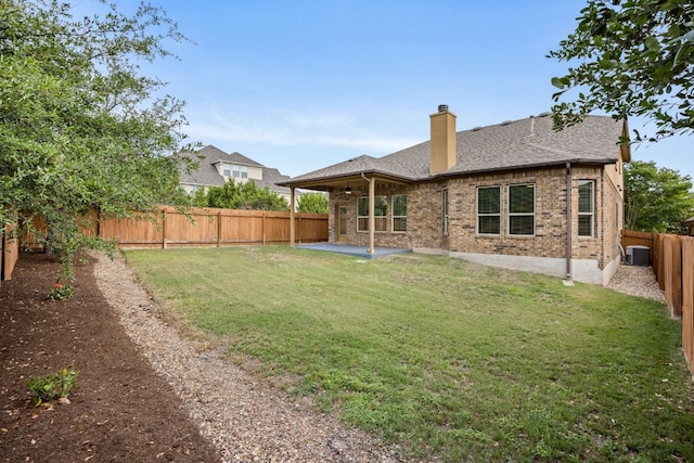 rear view of property featuring a chimney, a lawn, brick siding, a fenced backyard, and a patio