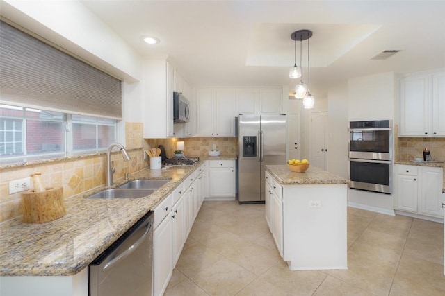 kitchen with decorative backsplash, a kitchen island, white cabinetry, a sink, and appliances with stainless steel finishes
