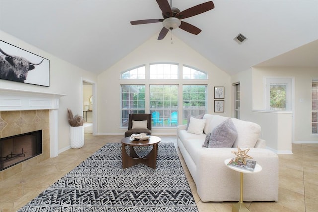 living area with visible vents, baseboards, high vaulted ceiling, a tiled fireplace, and a ceiling fan