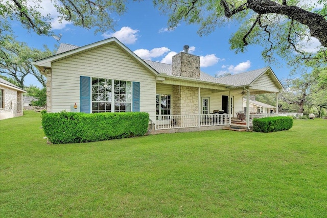 rear view of property featuring a lawn, a chimney, and a porch