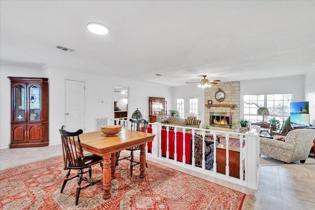 dining room featuring a ceiling fan, a stone fireplace, and visible vents