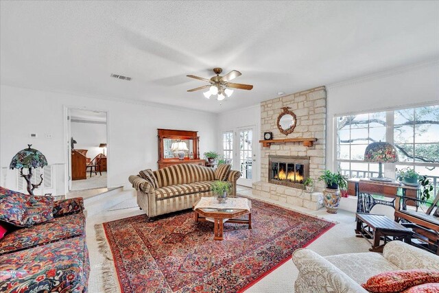 carpeted living room featuring crown molding, visible vents, a stone fireplace, ceiling fan, and a textured ceiling