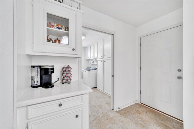 interior space featuring light countertops, washer / clothes dryer, white cabinets, and glass insert cabinets