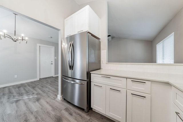 10429 Firethorn Ln, Austin, TX 78750 - kitchen with white cabinets, a notable chandelier, freestanding refrigerator, light wood-type flooring, and backsplash