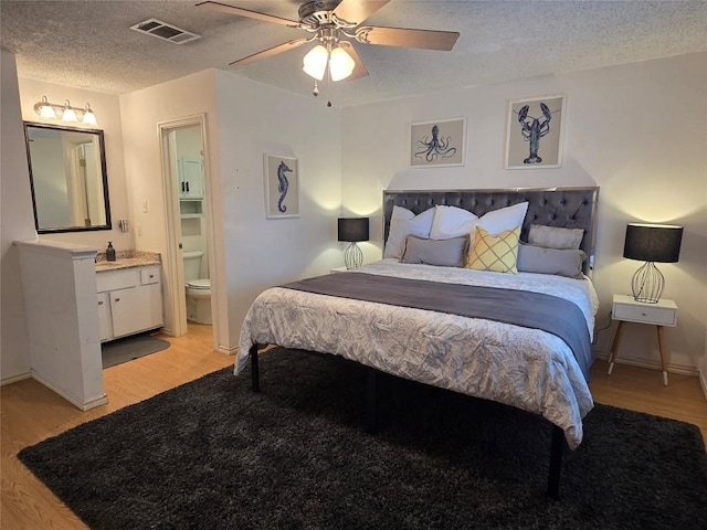bedroom with a textured ceiling, visible vents, baseboards, light wood-style floors, and ensuite bathroom