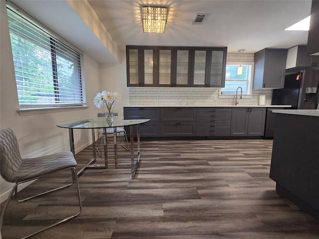 kitchen featuring black fridge with ice dispenser, glass insert cabinets, dark wood-style floors, light countertops, and backsplash