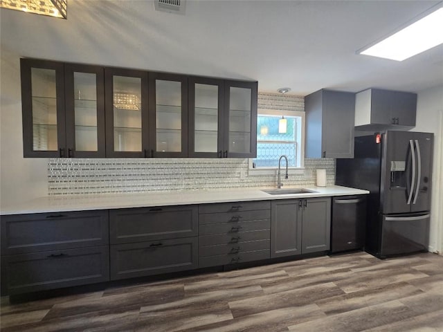 kitchen featuring a sink, black refrigerator with ice dispenser, backsplash, stainless steel dishwasher, and visible vents