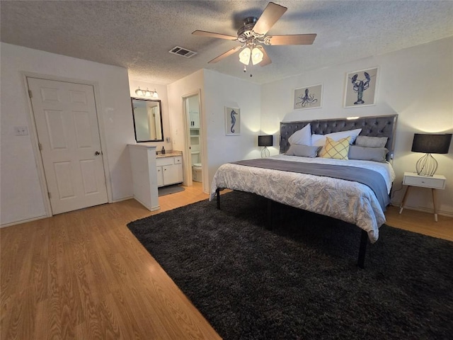 bedroom with visible vents, a textured ceiling, ensuite bath, and light wood-type flooring