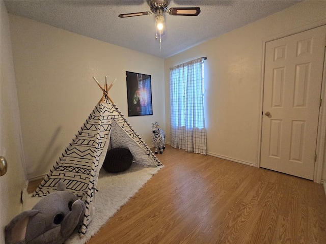 recreation room featuring a textured ceiling, ceiling fan, and wood finished floors