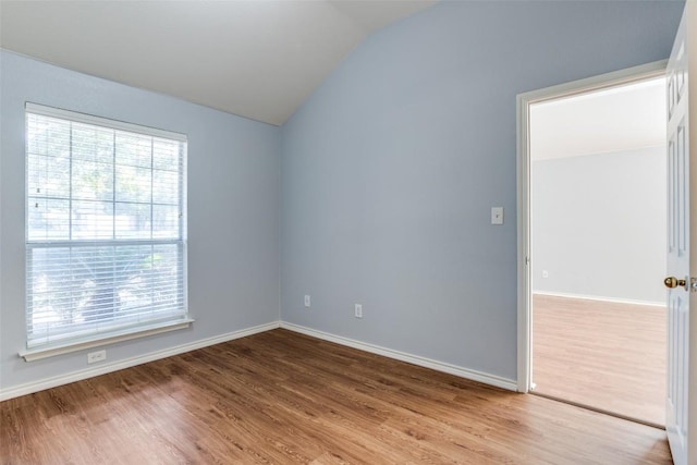 empty room with baseboards, vaulted ceiling, a wealth of natural light, and wood finished floors