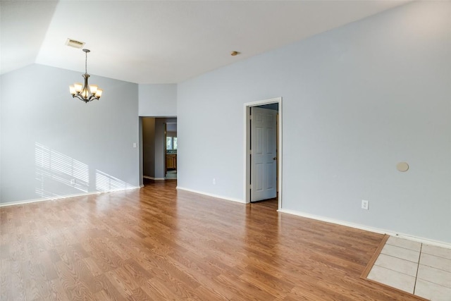 empty room with visible vents, vaulted ceiling, baseboards, an inviting chandelier, and light wood-style flooring