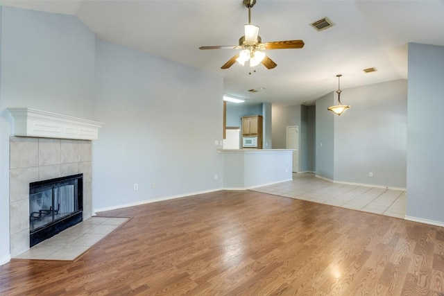 unfurnished living room with a ceiling fan, visible vents, light wood finished floors, and a tile fireplace