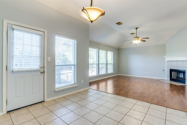 unfurnished living room with visible vents, lofted ceiling, a tiled fireplace, a ceiling fan, and light tile patterned floors