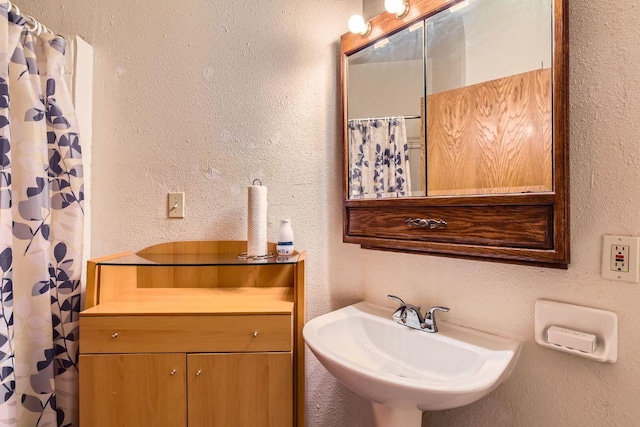 bathroom featuring a shower with shower curtain, a textured wall, and a sink