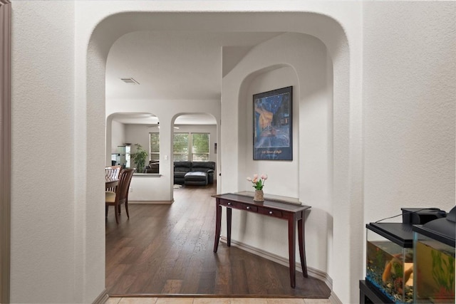 corridor featuring arched walkways, a textured wall, visible vents, and wood finished floors