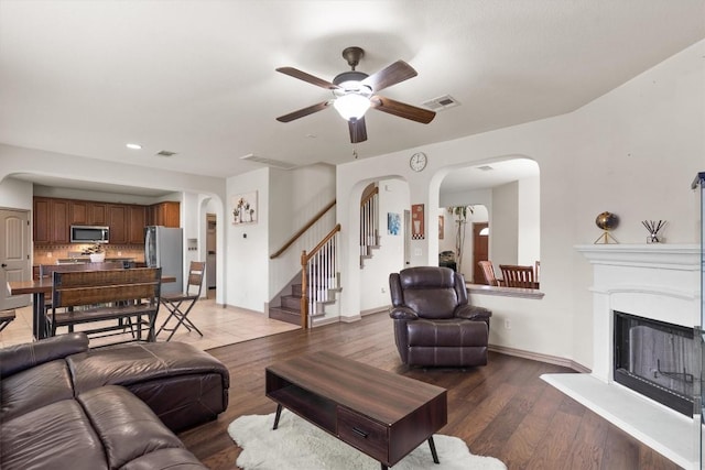 living room featuring visible vents, arched walkways, stairs, and a ceiling fan
