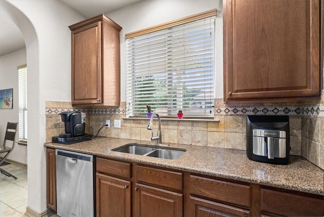 kitchen with arched walkways, decorative backsplash, a sink, and dishwasher