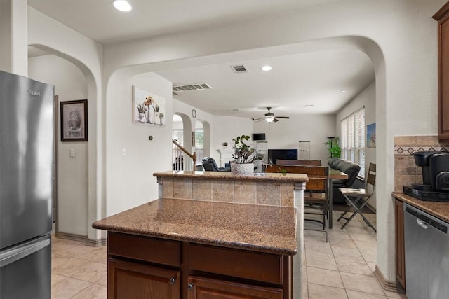 kitchen featuring ceiling fan, a kitchen island, arched walkways, light tile patterned floors, and stainless steel appliances