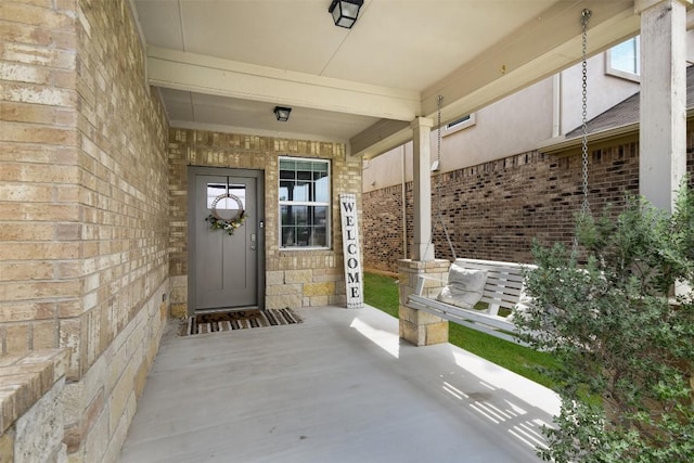 property entrance featuring brick siding, covered porch, and stone siding
