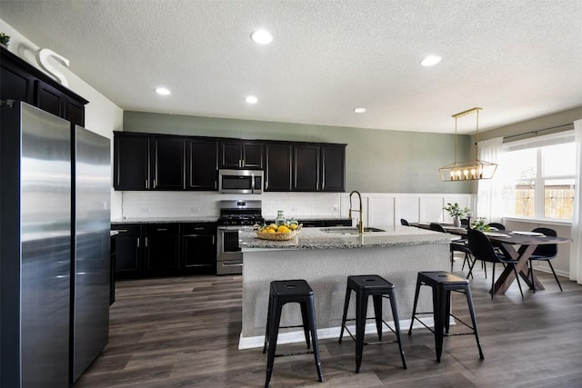 kitchen featuring dark wood-style flooring, a textured ceiling, a sink, dark cabinets, and stainless steel appliances