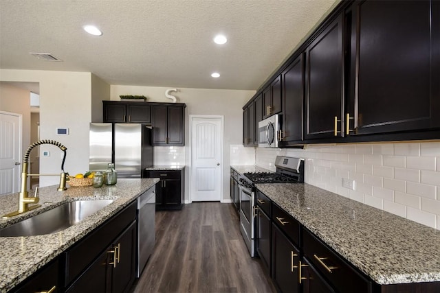 kitchen with dark wood-style flooring, appliances with stainless steel finishes, light stone counters, a sink, and backsplash