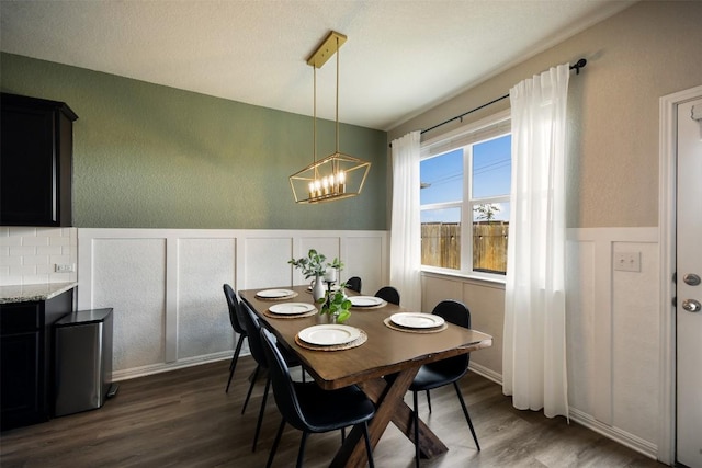 dining area featuring a decorative wall, a notable chandelier, wood finished floors, and a wainscoted wall