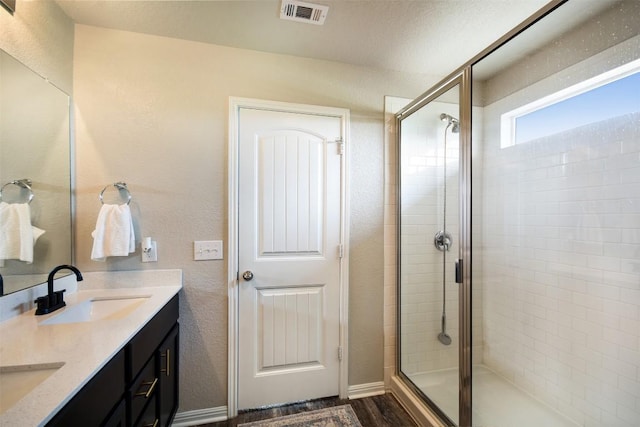 full bath featuring a sink, double vanity, wood finished floors, visible vents, and a stall shower