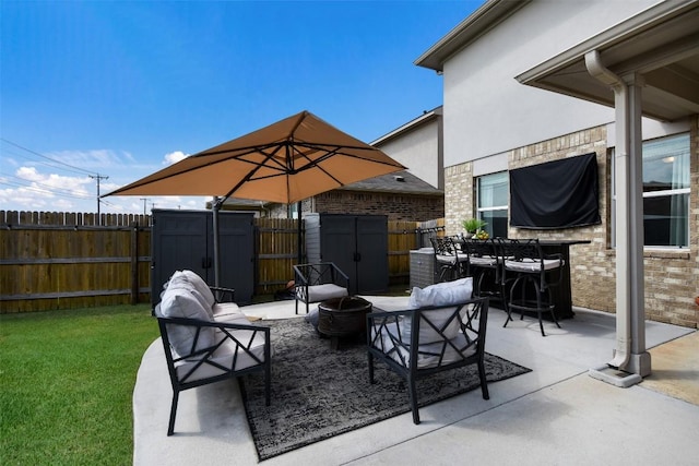 view of patio with an outbuilding, a gate, a shed, a fenced backyard, and a fire pit