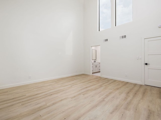 unfurnished room featuring a towering ceiling, baseboards, visible vents, and light wood-style floors