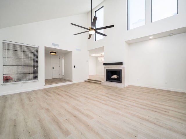 unfurnished living room with visible vents, a ceiling fan, light wood-style floors, and a towering ceiling
