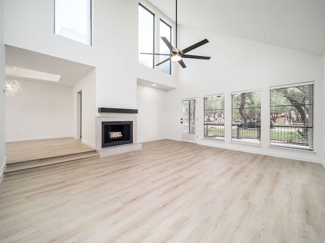 unfurnished living room featuring a ceiling fan, a towering ceiling, a skylight, wood finished floors, and a fireplace with raised hearth