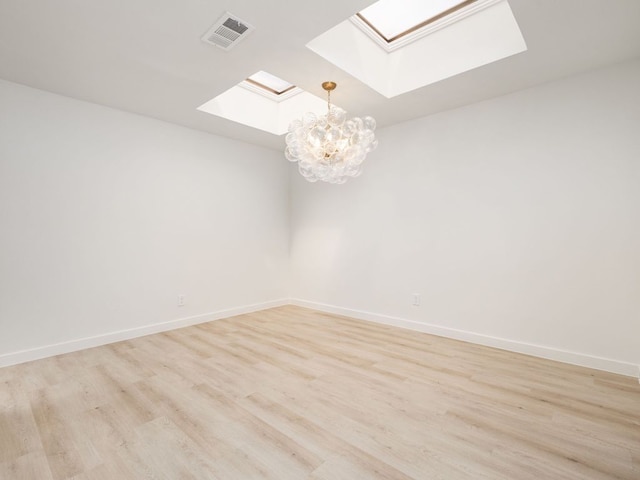 unfurnished room featuring a notable chandelier, a skylight, visible vents, and light wood-style floors