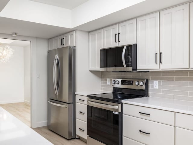 kitchen with decorative backsplash, light countertops, white cabinets, light wood finished floors, and stainless steel appliances