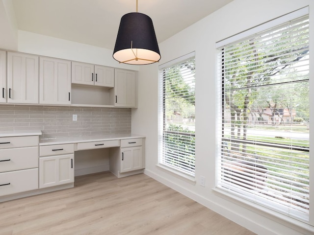 kitchen with built in desk, light countertops, light wood-style flooring, decorative light fixtures, and tasteful backsplash