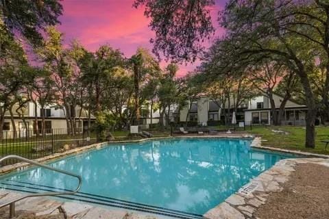 pool at dusk featuring a yard, a fenced in pool, and fence